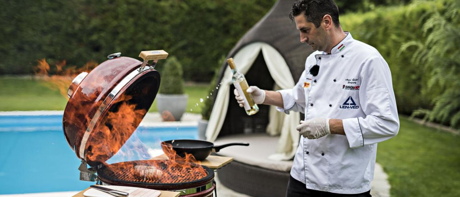 A chef cooking over open flame on a Kamado Chef beside the pool